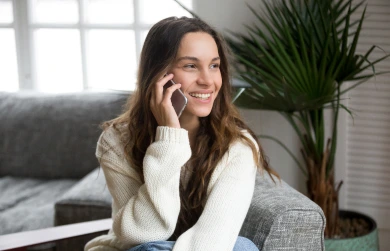 In a cozy and bright interior setting, a young woman is captured in a moment of pleasant conversation on her mobile phone.