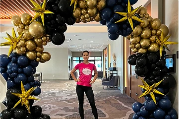 The image showcases a woman standing confidently in front of a grand balloon arch.