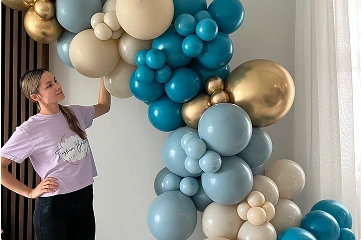 The image shows a woman admiring a large, colorful balloon arch.
