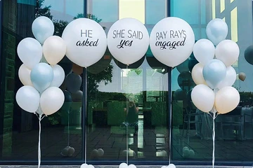 Several bunches of balloons are arranged in front of a glass building exterior.
